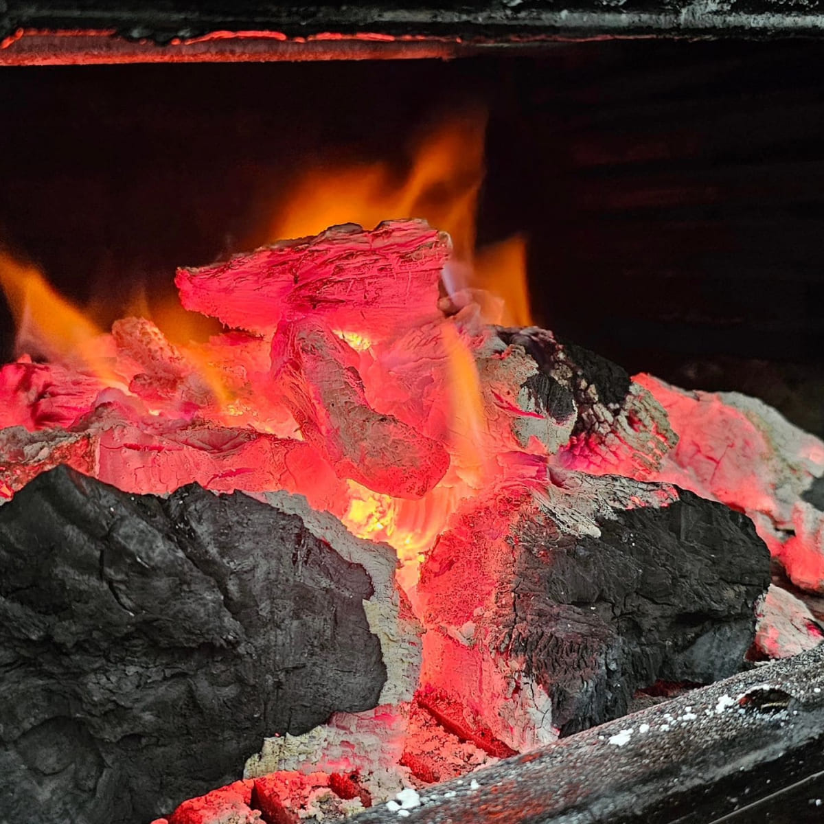 Vibrante imagen de brasas ardientes en la parrilla de Bilboburger, listas para cocinar hamburguesas con ese sabor ahumado único.