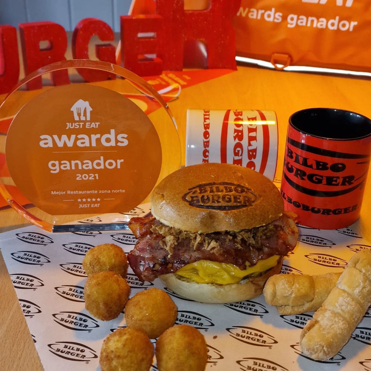 Galardón de Just Eat Awards 2021 mostrando a Bilboburger como ganador del Mejor Restaurante en la zona norte, junto a una hamburguesa, patatas y una taza con el logo