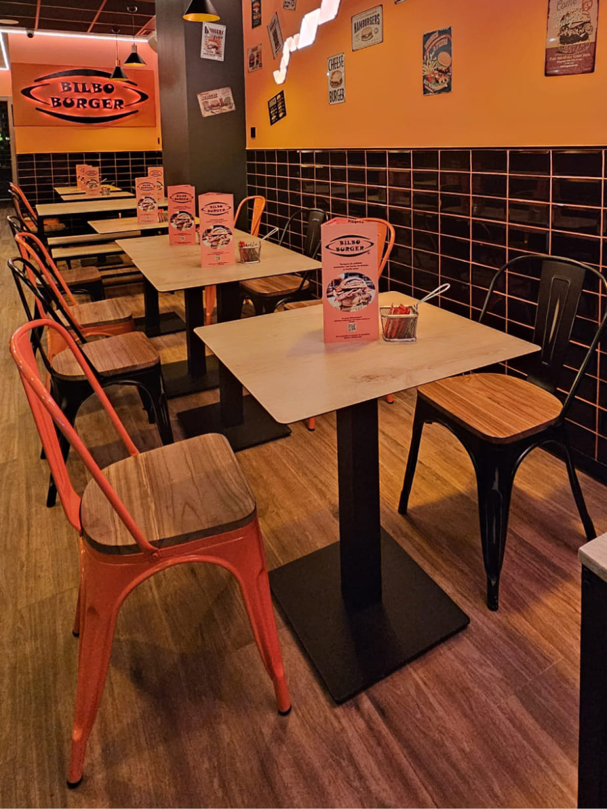 Interior de Bilboburger en Bilbao mostrando mesas de madera con sillas rojas y negras, menús sobre las mesas, y un vibrante ambiente con decoración temática de hamburguesas.